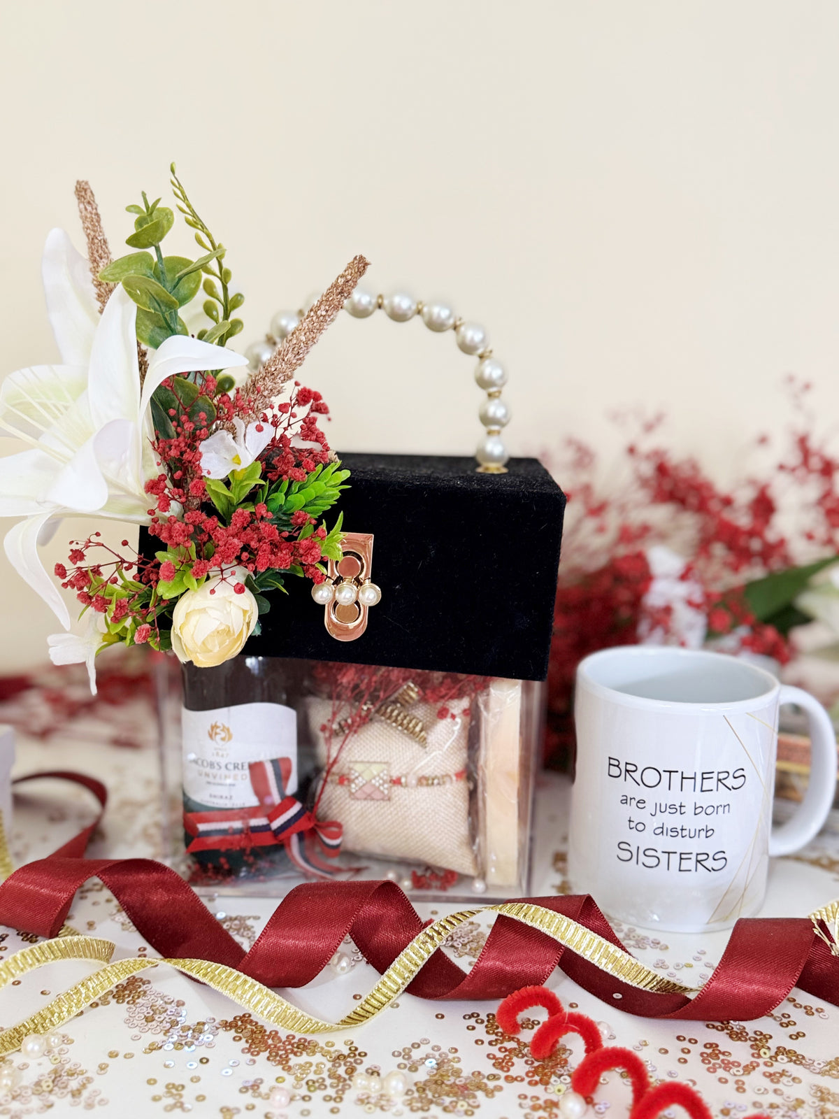 A gift set styled in a holiday theme, featuring a black velvet purse with a pearl handle, a floral arrangement, a bottle of scented oil, a mug that reads 'BROTHERS are just born to disturb SISTERS', and festive ribbons on a decorated table.